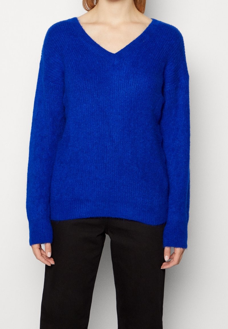 Pull bleu à col en V avec manches longues, fabriqué en matériau tricoté doux et texturé. Coupe décontractée, associé à un pantalon foncé. Aucun motif ou accent notable.