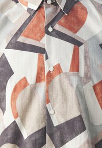 Camicia con bottoni caratterizzata da un motivo geometrico in tonalità tenui di rosso, grigio e crema. Realizzata in tessuto testurizzato con un colletto classico.