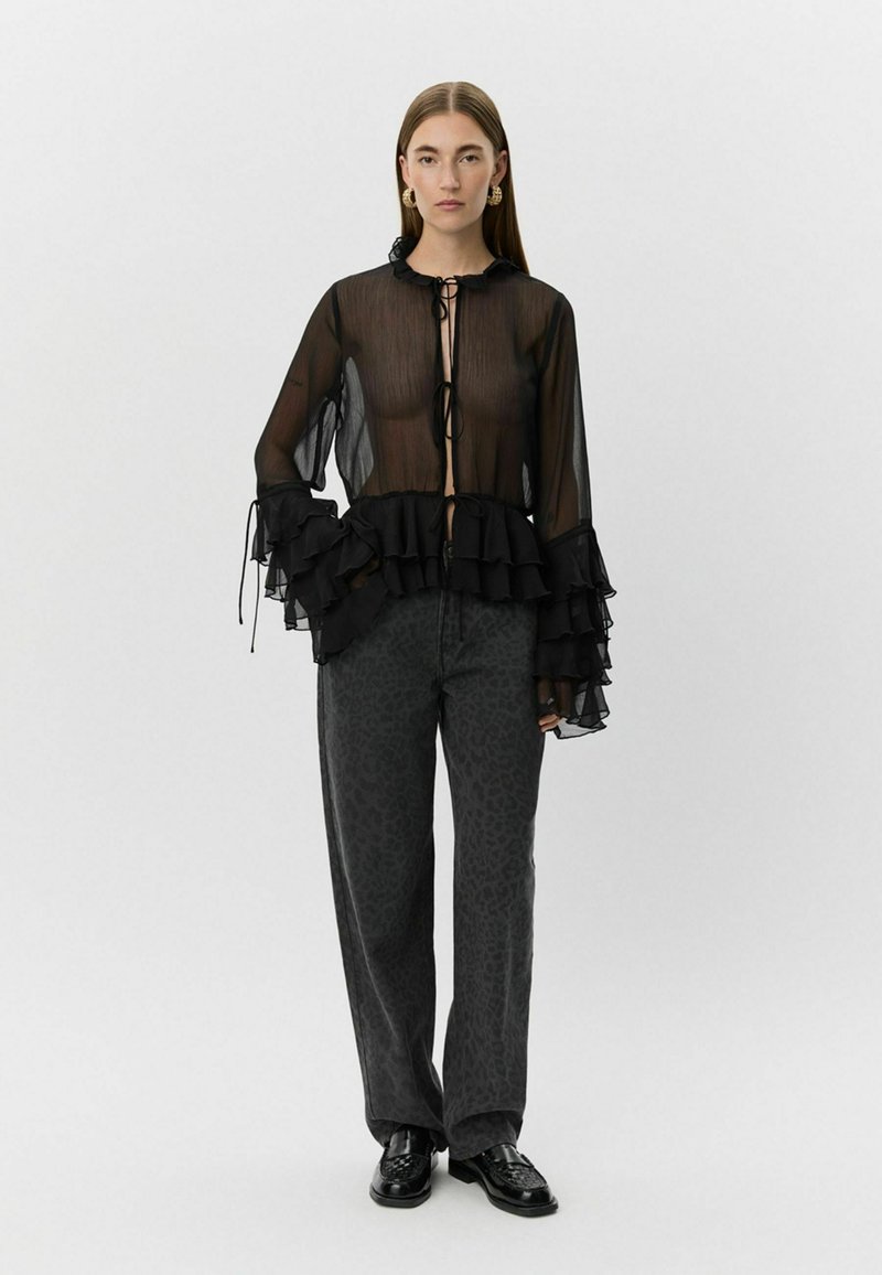 Black sheer blouse with ruffled sleeves and a tie-front closure, paired with dark gray leopard-print pants. Smooth fabric texture, loose fit.