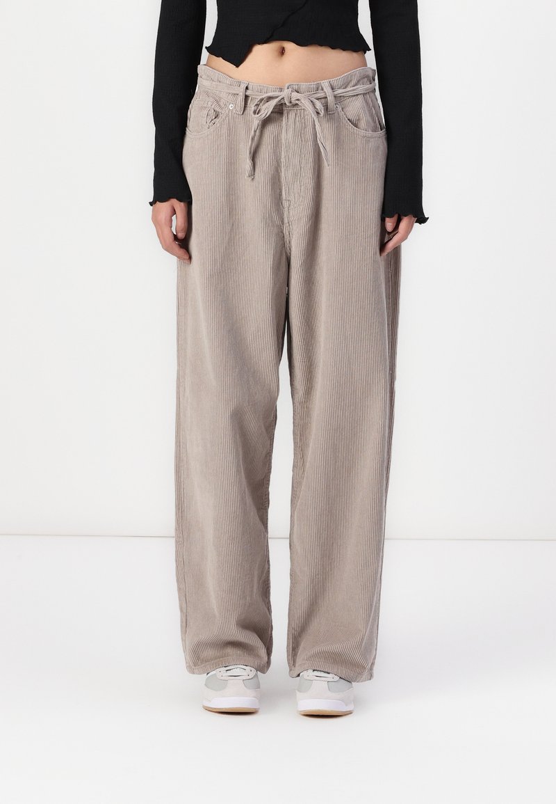 Pantalons en velours côtelé beige clair avec une coupe décontractée, dotés d'une taille à cordon de serrage, de poches latérales et d'une texture côtelée verticale.