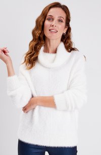 Witte, donzige gebreide trui met een coupenek, geribbelde manchetten en een details aan de zoom. Zachte textuur met een relaxte pasvorm, gedragen over donkere jeans.
