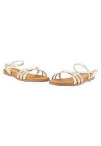 Sandalias planas de punta abierta con tiras trenzadas en color crema, plantilla en tono marrón y tiras delgadas en el tobillo. Presentan una suela de goma flexible para mayor comodidad.