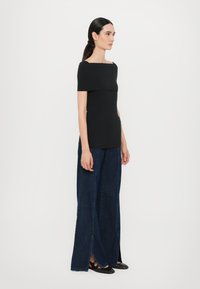 Zwart, nauwsluitend top met off-the-shoulder ontwerp, gecombineerd met wijde, donkere spijkerbroek met zijsplits. Materiaal lijkt glad en rekbaar.