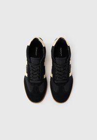Black athletic shoes with suede and fabric upper, featuring cream stripes, black laces, and a gum rubber outsole. GANT branding visible.