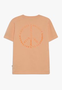Pfirsichfarbener Baumwoll-T-Shirt mit kurzen Ärmeln und einem kreisförmigen Grafikdesign mit dem Text "SCOTCH & SODA" in Orange, zentriert auf dem Rücken.