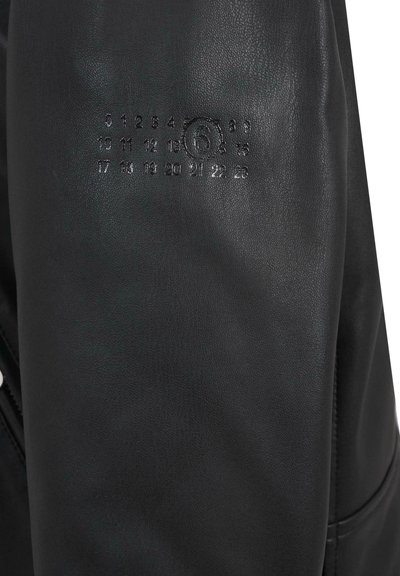 Veste en cuir noir avec une texture lisse, présentant des chiffres en relief sur la manche et une fermeture éclair. Design simple avec des accents minimaux.