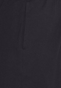 Close-up of dark fabric showing a vertical seam and partial pocket opening, highlighting texture and stitching details.