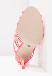 Rosa glittrande högklackad sko med öppen bak och smal stilett. Slät sula med textur och detaljerad remdesign synlig nedifrån.