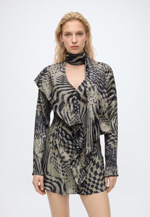Femme portant une mini-robe à manches longues à volants et une écharpe assortie avec un motif animal abstrait noir et vert olive.