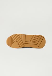 Bruine rubberen zool met geometrische patronen en getextureerde ribbels. Bevat branding aan de zijkant, ontworpen voor grip en duurzaamheid.