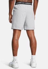 Pantalones cortos deportivos de color gris claro con dobladillo perforado, cinturilla elástica con un logo negro. Zapatillas blancas y calcetines hasta el tobillo visibles.