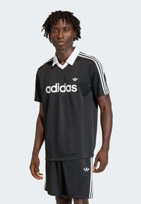 Σετ μαύρης φανέλας και σορτς Adidas με λευκές ρίγες, με γιακά και λογότυπο. Κατασκευασμένο από διαπνέον υλικό, προσφέροντας εφαρμοστή σχεδίαση.