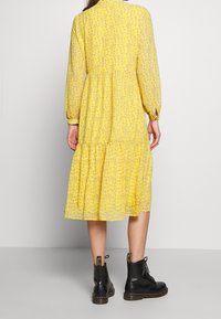 Vestido floral amarillo con mangas largas, dobladillo en capas y tejido suave y translúcido, combinado con botas negras con cordones.