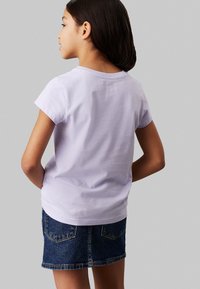 Camiseta de algodón lavanda de manga corta combinada con una falda corta de mezclilla. La camiseta tiene un cuello redondo y una textura suave.