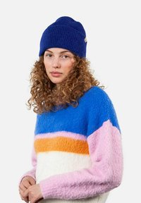 Knitted blue beanie with folded cuff; fuzzy, multicolored sweater featuring blue, pink, orange, and white horizontal stripes.