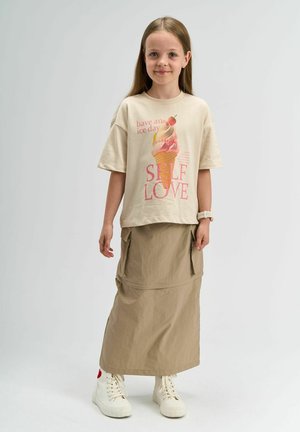 Beige t-paita, jossa on jäätelökuva vaaleanpunaisena ja oranssina sekä teksti. Yhdistetty pitkän khaki-hameen ja valkoisten nilkkuritennareiden kanssa.