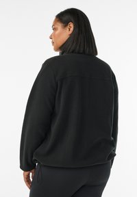 Sweatshirt en polaire noir à coupe décontractée, avec un col rond et une couture décorative dans le dos. Le tissu est doux et a une texture lisse.