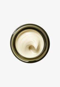 Tykk, kremet fuktighetskrem i et rundt glasskrukke med mørkegrønt lokk. Jevn, offwhite tekstur som virvler langs kanten inne i beholderen.