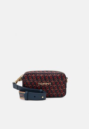 Sac bandoulière rectangulaire compact avec motif géométrique rouge et noir, lettrage doré "TOMMY" et sangle bleu marine réglable avec détail de marque.
