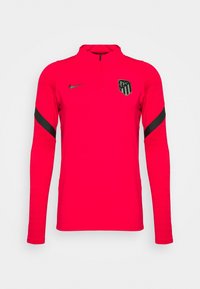 Camiseta atlética roja de manga larga con cuello de media cremallera, logo negro de Nike y un emblema en el pecho izquierdo, tejido texturizado y mangas ajustadas.