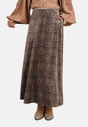 Mujer con una falda larga marrón con estampado de paisley, una blusa beige con mangas abullonadas y botines marrones con un patrón de piel de serpiente en la punta.