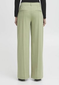 Helle grüne weit geschnittene Hose aus glattem Material, mit vorderen Falten und Gesäßtaschen. Abgeschlossen mit einem maßgeschneiderten Bund und Saum.