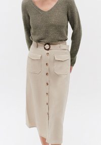 Jupe beige à mi-longueur avec une taille mi-haute, grandes poches latérales, une ceinture avec une boucle ronde et une fermeture à boutons à l'avant. Haut en maille texturée.