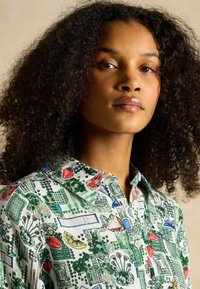 Cămașă din bumbac cu un imprimeu botanic multicolor în verde, roșu și albastru; are guler în vârf și închidere cu nasturi.