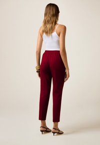 Rode, taps toelopende broek met een elastische tailleband, gemaakt van een gladde stof. Gecombineerd met een witte tanktop en zwarte enkelband sandaaltjes.