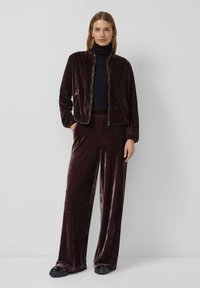 Pluche, diep bordeaux fluwelen jasje met een rits aan de voorkant en elastische manchetten, gecombineerd met bijpassende broek met brede pijpen en een zwarte coltrui.