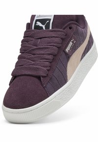 Ljubičaste suede tenisice s teksturiranim uzorkom krokodila, s širokim vezicama i bijelim gumeni potplat. PUMA logo na jeziku i bočnoj strani.