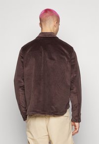 Brun kordjacka med en strukturerad yta, knäppte ärmslut och krage. Baksidan har en sömdetalj och en avslappnad passform.