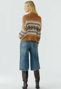 Gebreide bruine en crèmekleurige gebloemde trui, gecombineerd met hoge blauwe denim culottes en bruin kniehoog laarzen.