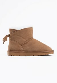 Stivaletti alla caviglia beige in suede con una morbida fodera in pelliccia sintetica bianca, caratterizzati da un design avvolgente e un accento con nappe sul retro. Suola piatta in gomma.