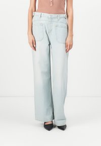 Lichtblauwe wijde jeans van denim, met een hoge taille, twee achterzakken en een licht vervaagde afwerking. Gecombineerd met zwarte hakken.