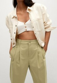 Chemise oversize beige clair, top blanc court avec des boutons, et pantalon taille haute vert clair. Tissu lisse, coupe décontractée, design minimal.