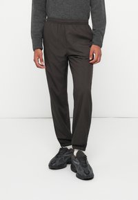 Dunkle, leichte, elastische Hosen mit schmalen Bündchen, getragen mit schwarzen Sportschuhen; glattes, wasserabweisendes Material.