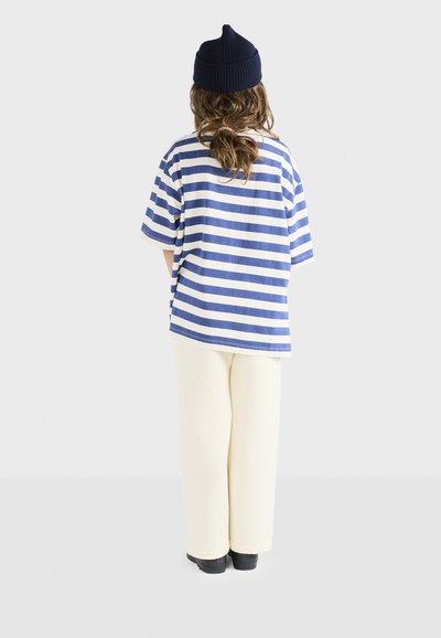Blå og hvidstribet t-shirt med afslappet pasform, sat sammen med cremefarvede bukser med vide ben; stylet med en marineblå hue og sorte sko.