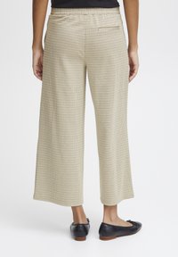 Pantalon large en plaid beige avec taille élastique, poche arrière et texture lisse, associé à des ballerines noires.