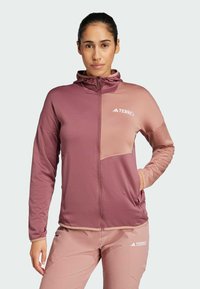 Rosa och lilat zip-up jacka med en huva, som har ett texturerat mönster och en bröstficka. Varumärket "TERREX" är tydligt synligt.