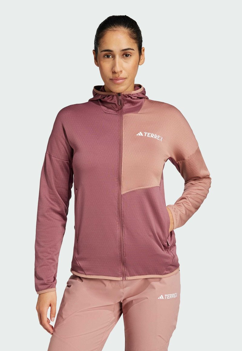 Rosa och lilat zip-up jacka med en huva, som har ett texturerat mönster och en bröstficka. Varumärket "TERREX" är tydligt synligt.