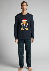 Námořnická mikina má grafiku perníkového muže se santovskou čepicí; kostkované pyžamové kalhoty v zelených a modrých odstínech; casual, měkká tkanina.