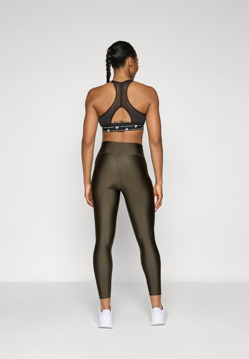 Schwarzer Sport-BH mit Racerback-Design und Ausschnitt-Detail, kombiniert mit hochgeschnittenen olivgrünen Leggings, getragen mit weißen Turnschuhen.