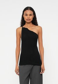 Svart one-shoulder topp med strukturert strikket design. Tett silhuett, ribbestrikket mønster og glatt overflate, kombinert med løse grå bukser.