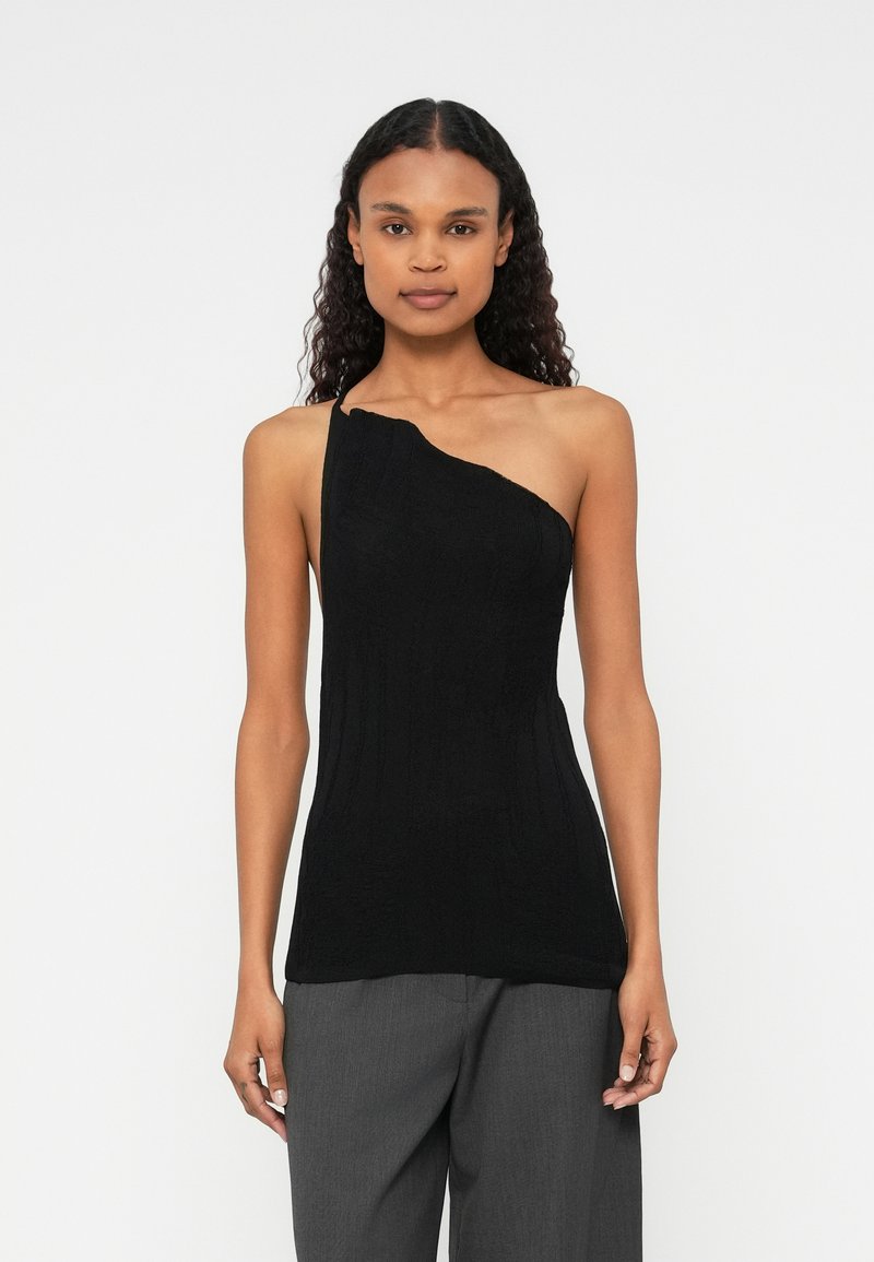 Svart one-shoulder topp med strukturert strikket design. Tett silhuett, ribbestrikket mønster og glatt overflate, kombinert med løse grå bukser.
