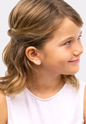 Studørering formet som en lille pink skal, båret af et barn med bølget lysebrunt hår, iført en hvid ærmeløs top.