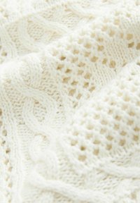 Tessuto lavorato a maglia color crema con motivi alternati a trecce e trafori, che mostrano trama e morbidezza.