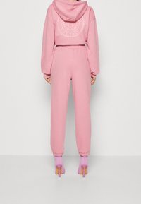 Conjunto de sudadera rosa claro y joggers, con un logo en la parte de atrás, y mangas y tobillos con puños. Combinado con calcetines rosas con estampado y tacones.
