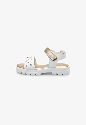 Sandalo bianco con dettagli in tonalità oro, una fascia larga con borchie decorative e una chiusura regolabile in Velcro su suola in gomma bianca.