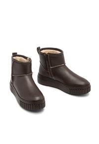 Botas de cuero marrón hasta el tobillo con forro de felpa, cremallera lateral y suela de goma texturizada; cuenta con costuras decorativas a lo largo de la parte superior.